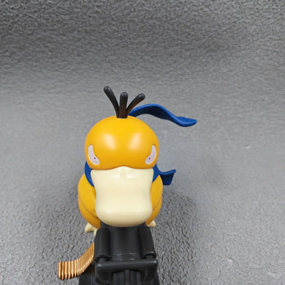 Yellow duck-like figurine with a blue scarf, holding a black Gatling gun, viewed from above.