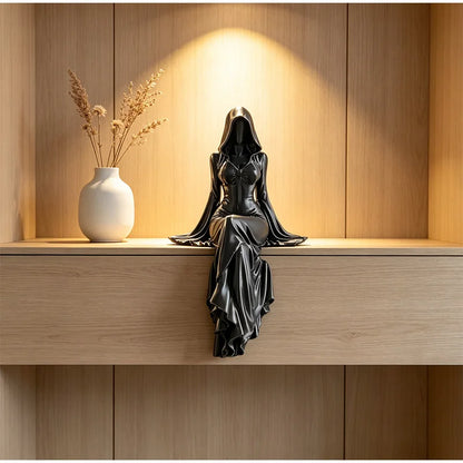 A black hooded female figure statue sits on a wooden shelf, her long skirt cascading down.