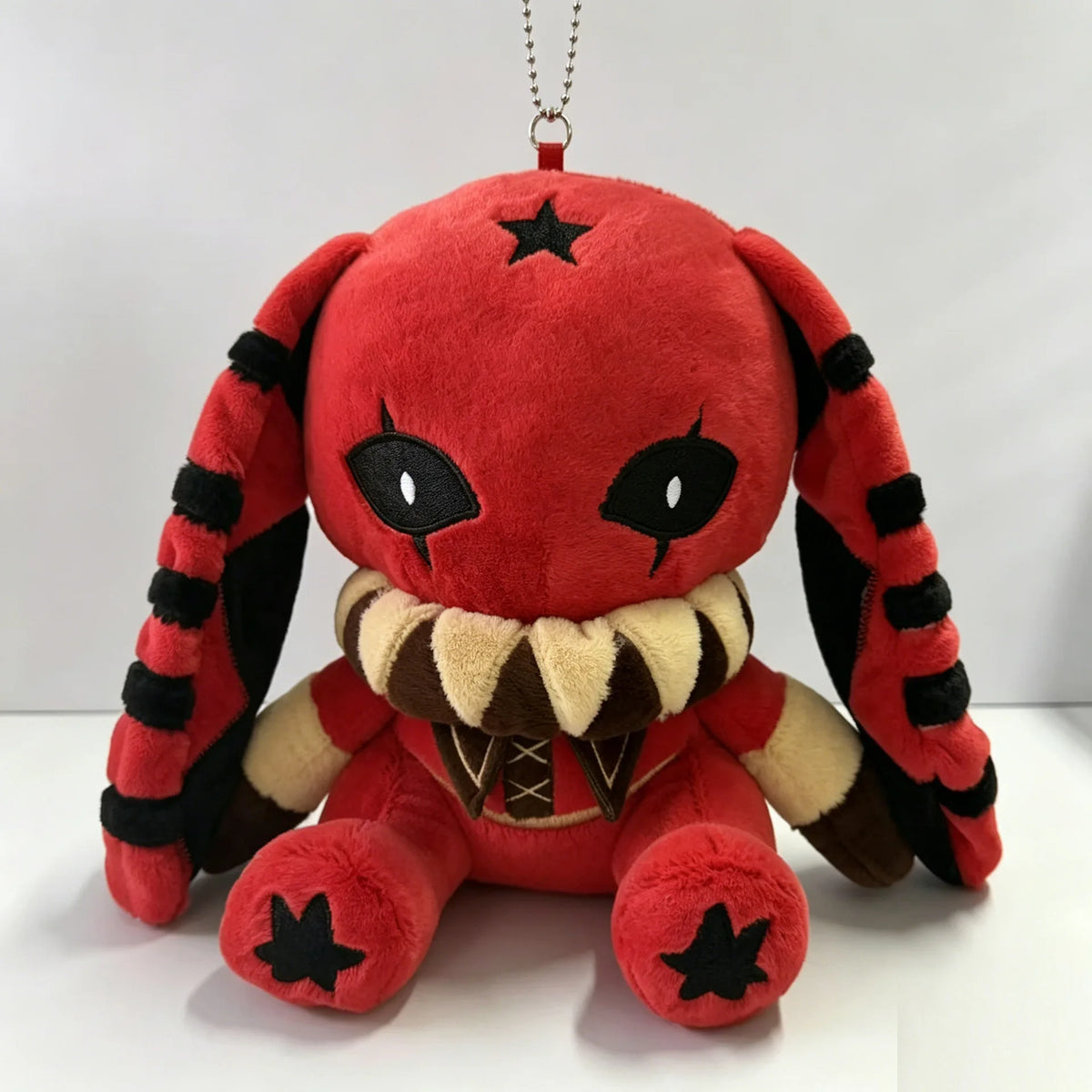 A red Pierrot rabbit plush toy with black-striped ears, large fanged collar, and a black star on its head.