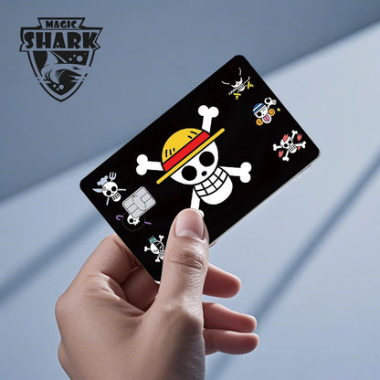 A hand holds a black card skin featuring a large white skull and crossbones wearing a yellow and red straw hat.