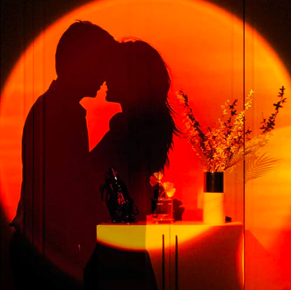 Silhouette of a couple facing each other against a large, bright orange sunset lamp projection on a wall.