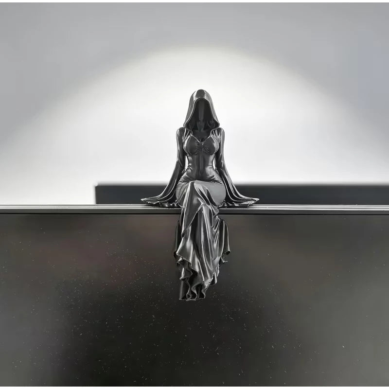 A black figurine of a hooded woman in a fitted dress sitting and dangling her legs.