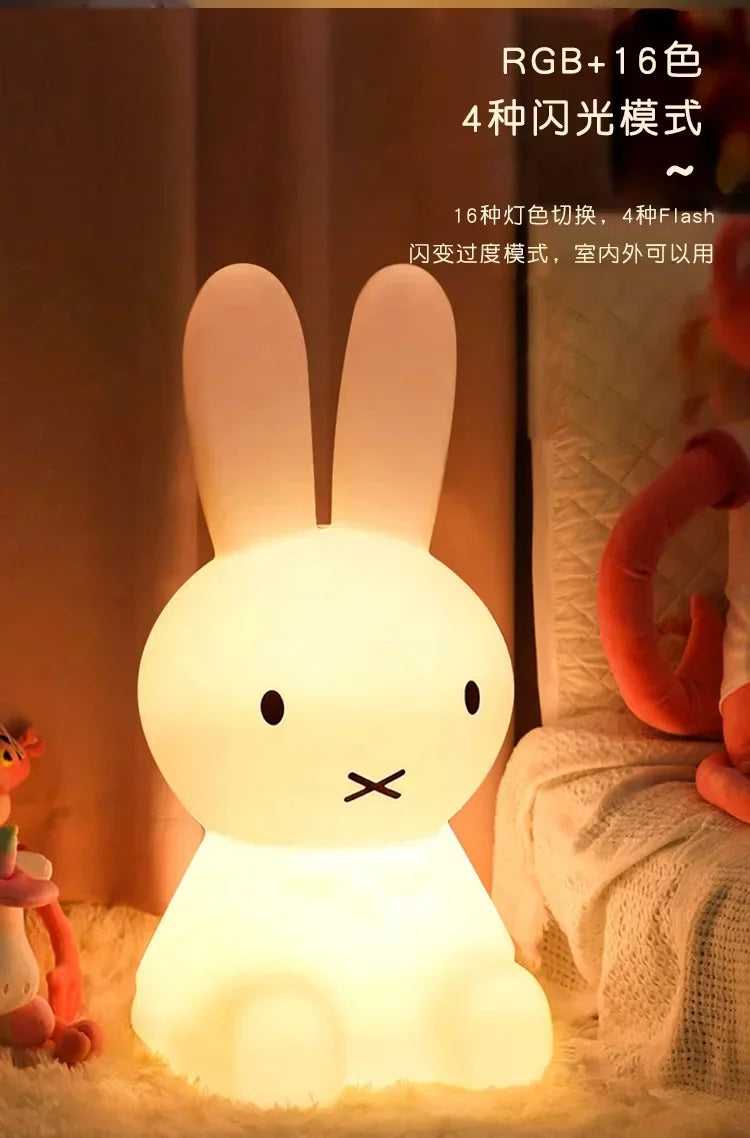White glowing Miffy rabbit night light with a round head, long upright ears, and a cross-shaped mouth, sitting on a soft surface.