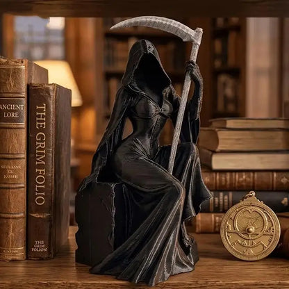 A black resin figurine of a hooded female Grim Reaper holding a silver-bladed scythe, sitting among books.