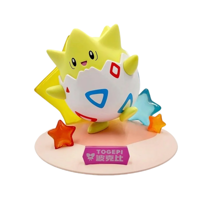 Togepi figure in a white-and-red-patterned eggshell on a pink base with translucent stars and a "TOGEPI" sign.