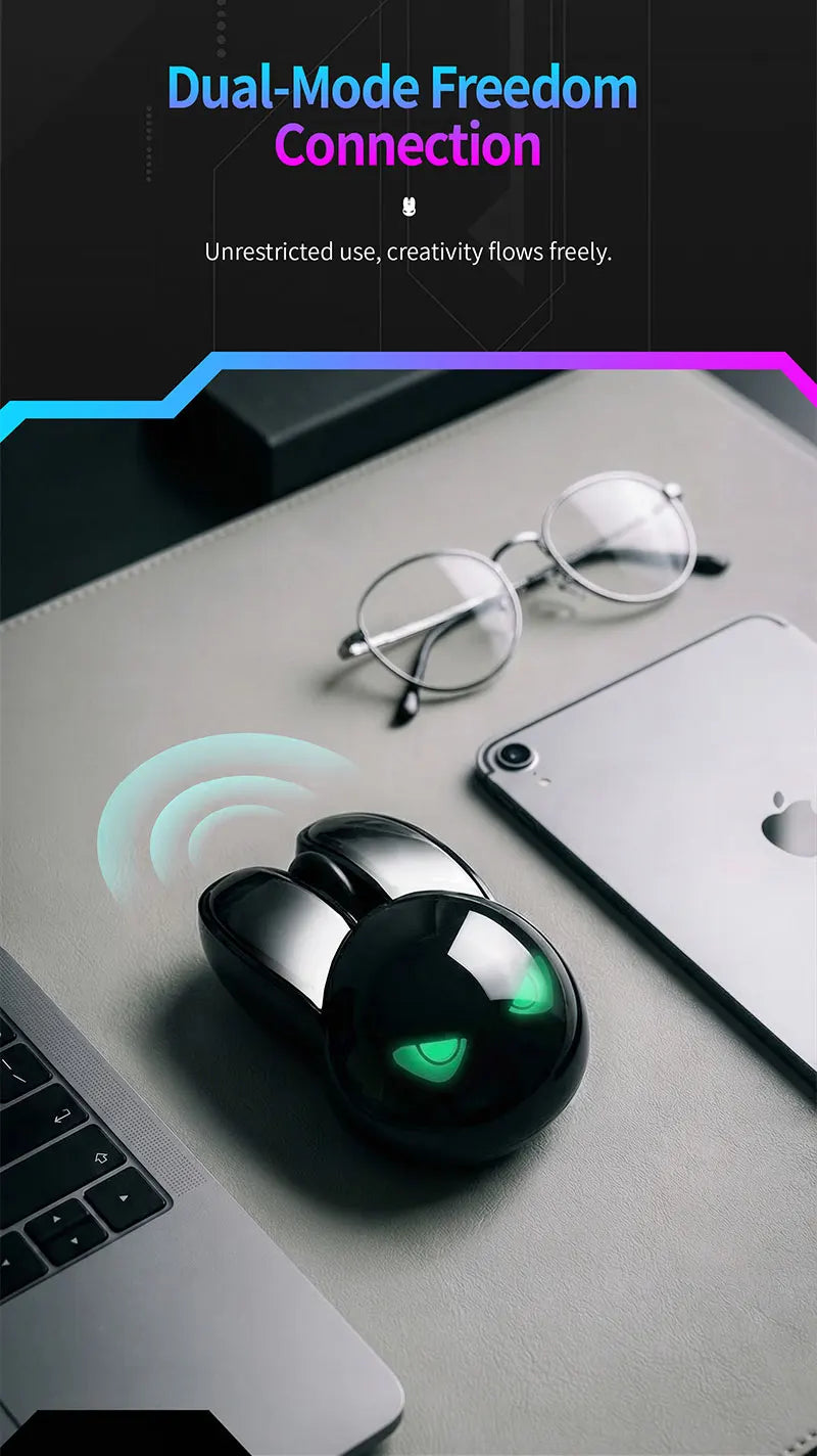 Black MOFII M6C rabbit-shaped wireless mouse with glowing green eyes on a desk with glasses and a tablet.
