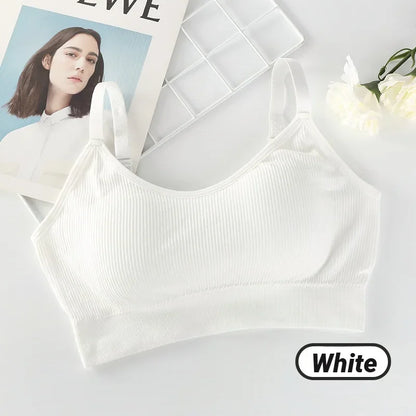 A ribbed white seamless bralette with adjustable straps, displayed with white flowers and a magazine.