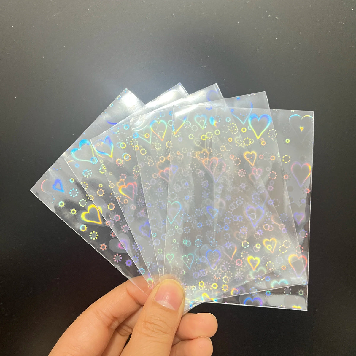 Fanned clear card sleeves with holographic laser heart and flower patterns.