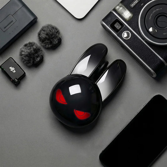 Black rabbit-shaped wireless mouse with glowing red eyes, surrounded by electronics on a gray surface.