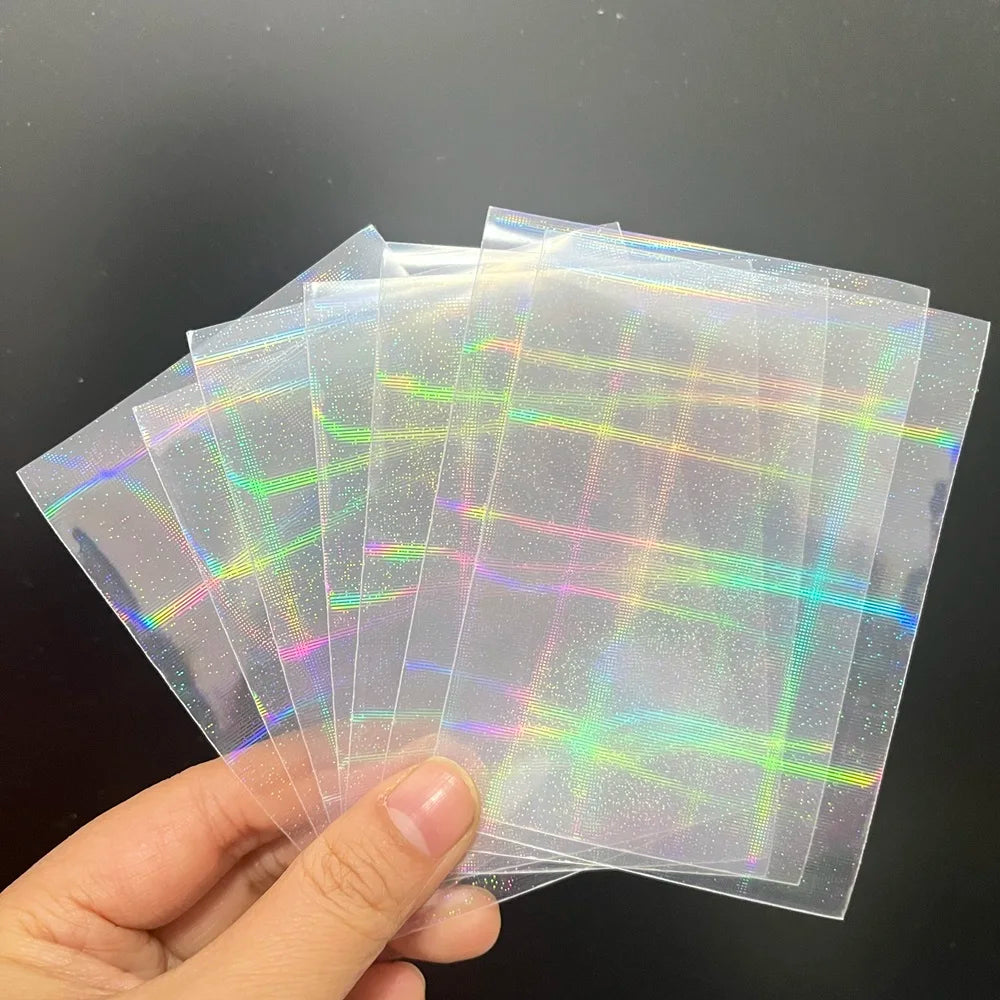 A hand holds a fan of clear trading card sleeves with a holographic laser grid and sparkle pattern.