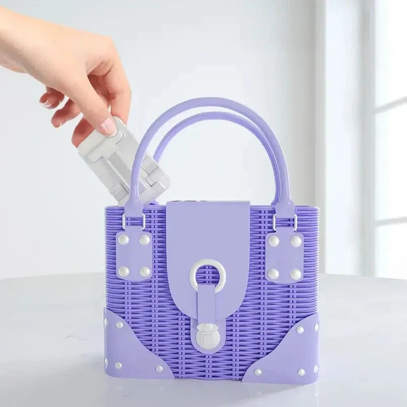 A hand places a white, foldable phone and tablet stand into a purple, woven handbag.
