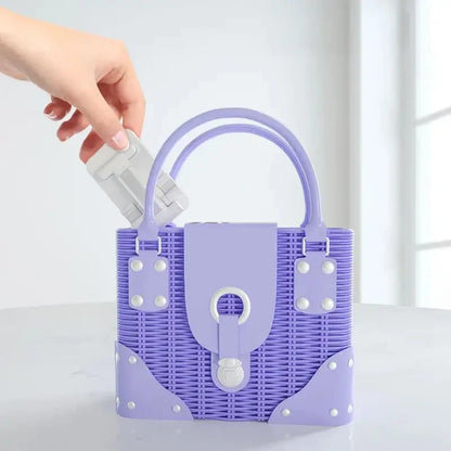 A hand places a white, foldable phone and tablet stand into a purple, woven handbag.
